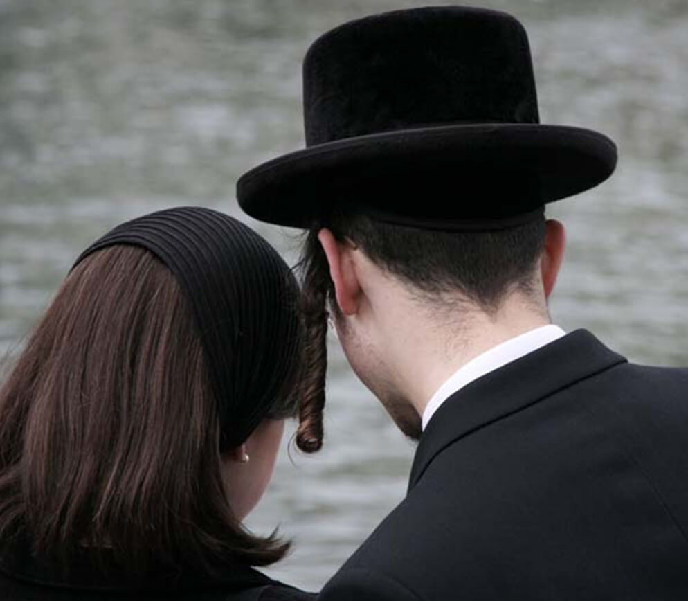 A couple dressed in black stands by the water's edge